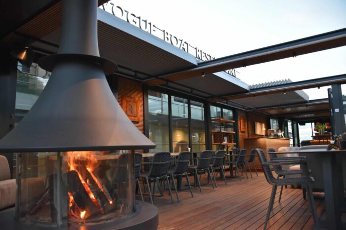 Fatüzelésű kandalló tüze a Vogue étteremhajó fedélzetén, kényelmes székekkel a háttérben.