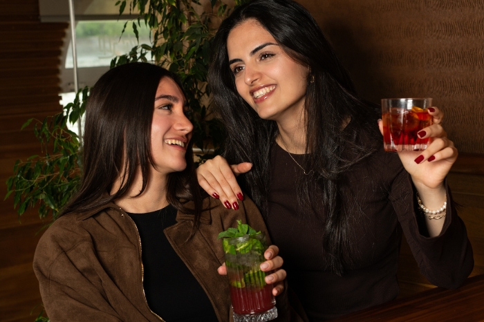 Two friends cheerfully chatting and enjoying delicious signature cocktails in the elegant interior of the Vogue Boat Restaurant in Budapest.